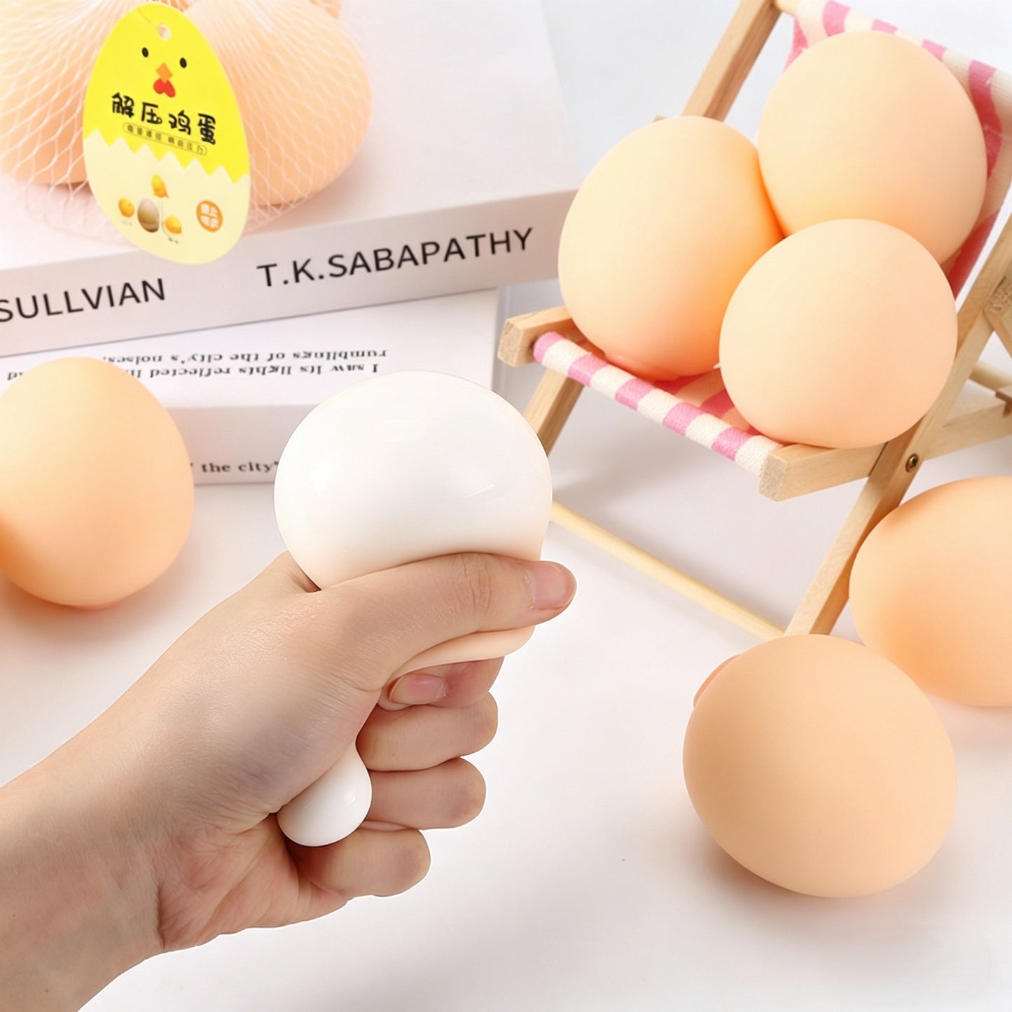 "Multiple realistic egg squishy toys arranged on a wooden chair and books"