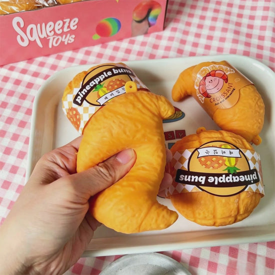 "Hand squeezing realistic croissant squeeze toy showing soft and chewy texture"